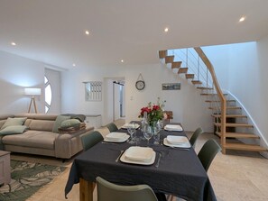 Un coin repas avec une table dressée pour quatre personnes, un escalier et un salon avec un canapé et une lampe.