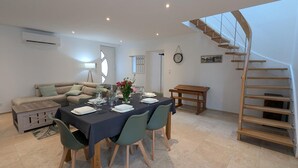 A dining area with a table set for four, a sofa, a wooden bench, and a spiral staircase. - House with AC in the heart of the village - 6 guests (SAINT SIMON)