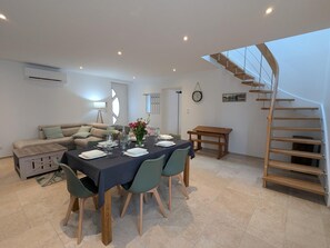 Un coin repas avec une table dressée pour quatre personnes, un canapé, un banc en bois et un escalier en colimaçon.