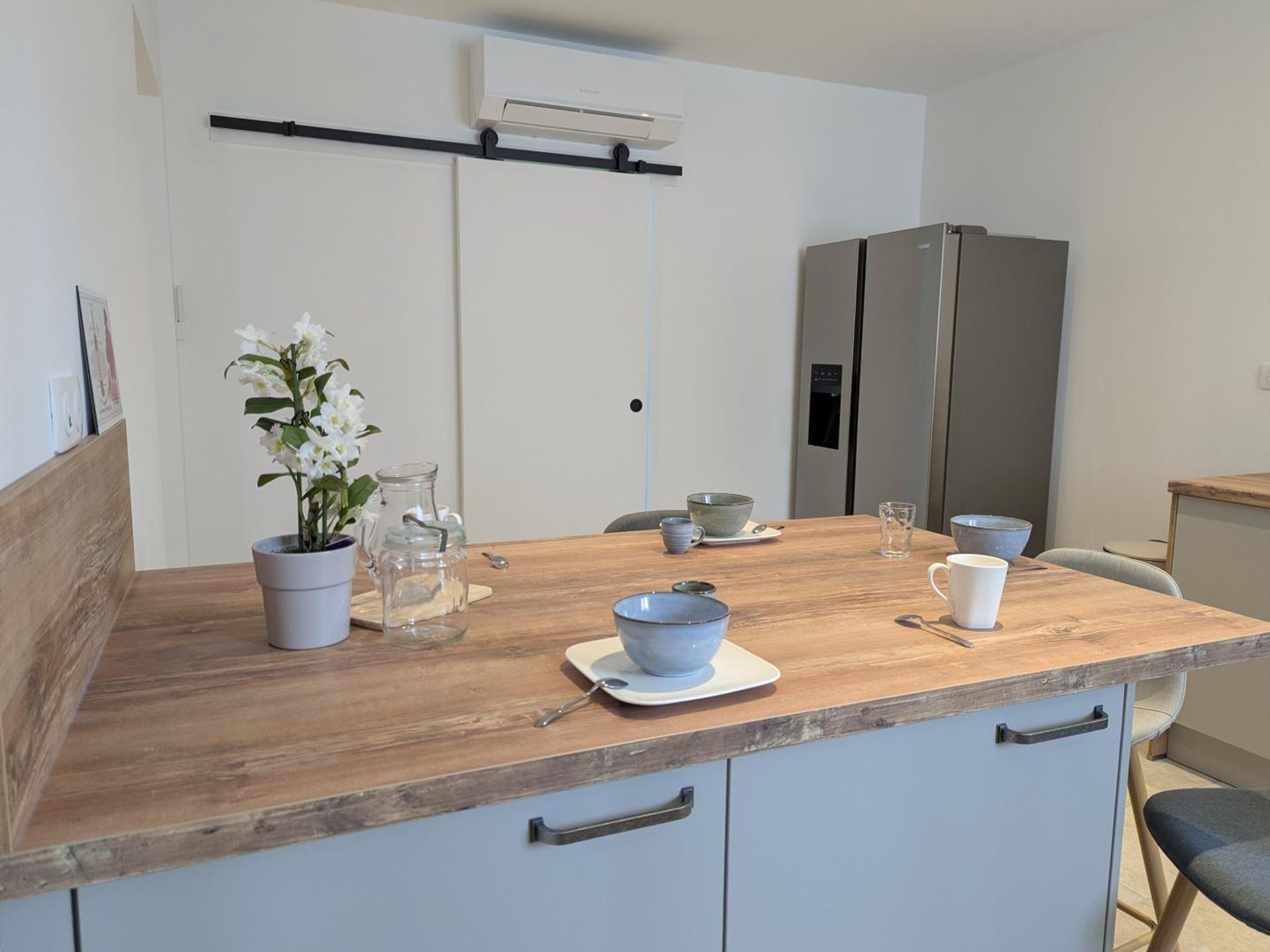 Een keuken met een houten aanrecht, een bloempot, een glazen karaf en een roestvrijstalen koelkast.
