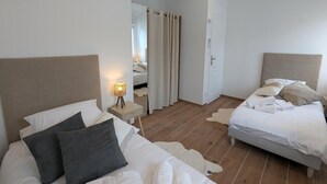 A bedroom with two beds, a nightstand with a lamp, a mirror, and a door leading to another room. - House with AC in the heart of the village - 6 guests (SAINT SIMON)