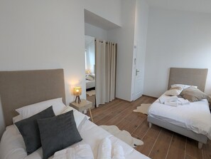 Une chambre avec deux lits, une table de chevet avec une lampe, un miroir et une porte donnant sur une autre pièce.