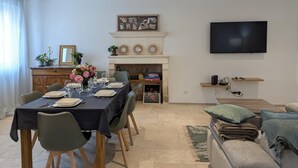A dining area with a table set for four, a fireplace, a television, and a sofa. - House with AC in the heart of the village - 6 guests (SAINT SIMON)