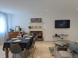 Un coin repas avec une table dressée pour quatre personnes, une cheminée, un téléviseur et un canapé.