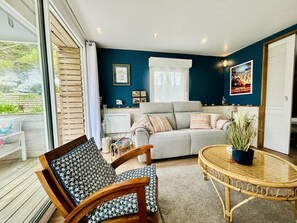 A cozy living room with a grey sofa, a wooden chair, a round wicker table, and a large window. - Cosy house near the sea - 2 guests (Barneville-Carteret)