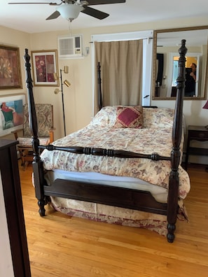 Una cama con dosel, colcha con estampado floral, ventilador de techo, espejo y un cuadro en la pared.