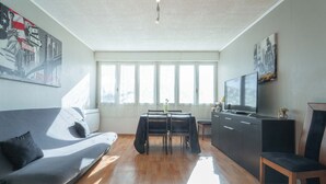 A modern living room with a sofa, a dining table with chairs, a TV, and artwork on the walls. - Apartment between ocean and forest - 6 guests (Mimizan)