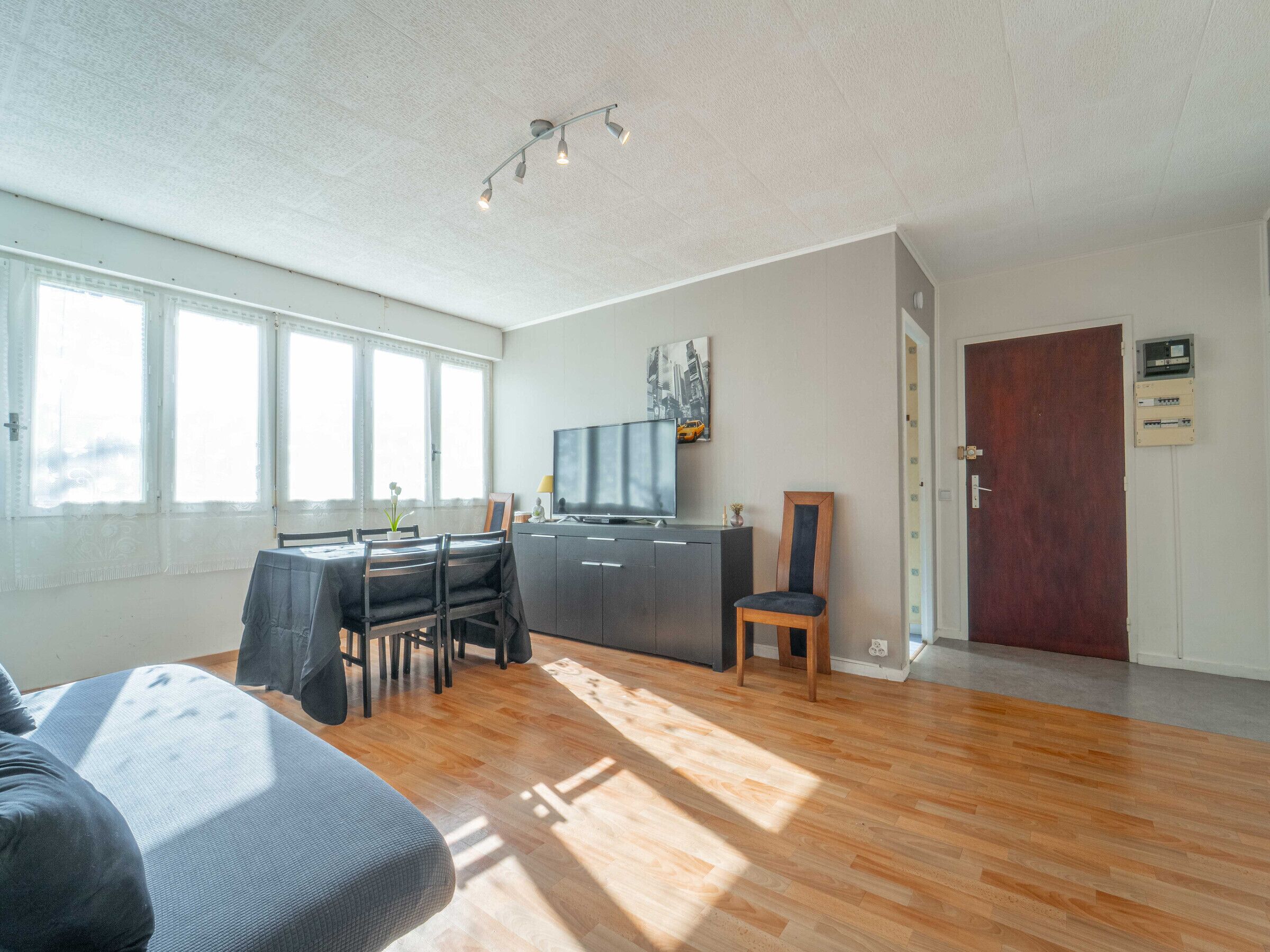 A spacious living area with a dining table, chairs, a sofa, a TV, and a wooden door.