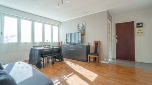 A spacious living area with a dining table, chairs, a sofa, a TV, and a wooden door. - Apartment between ocean and forest - 6 guests (Mimizan)
