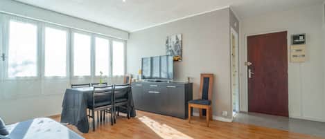 A spacious living area with a dining table, chairs, a sofa, a TV, and a wooden door.