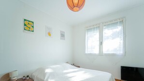 A bedroom with a bed, a wooden dresser, a bedside table, and a window with curtains. - Apartment between ocean and forest - 6 guests (Mimizan)