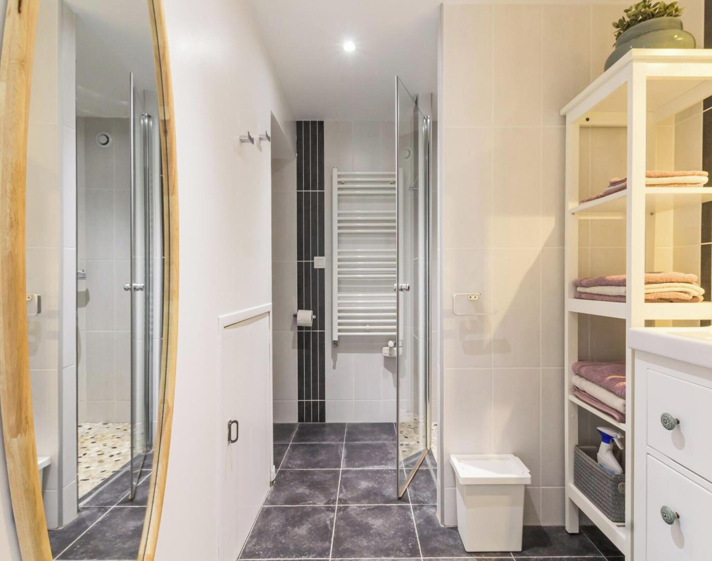 A bathroom with a glass shower enclosure, a white cabinet with towels, and a tiled floor.