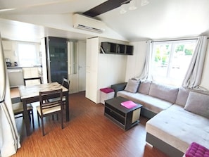A compact living space with a dining area, kitchenette, and a sofa with cushions. - Family mobile home with AC - 4 guests (Bourg-Charente)