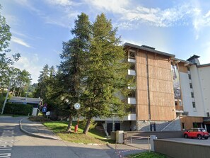 Ein mehrstöckiges Gebäude mit modernem Design, einem Parkplatz und einem roten Auto davor.