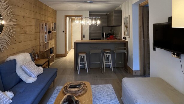 Uma sala de estar moderna com um sofá azul, uma mesa de centro de madeira e uma TV fixada na parede.