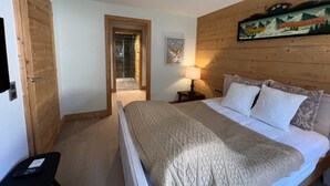 Um quarto com uma cama, uma porta de madeira, uma mesa pequena com abajur e um quadro na parede.