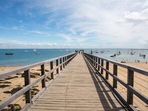 A wooden pier leading to a beach with boats in the water.
