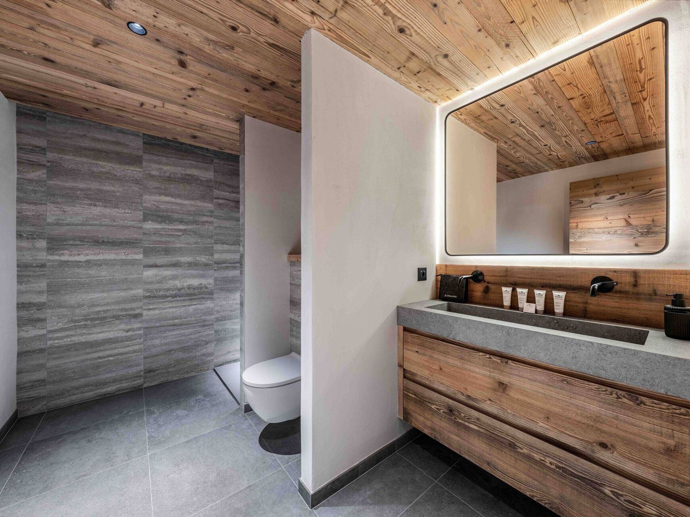 A modern bathroom with a wooden ceiling, a large mirror, a wooden vanity, and a shower area.