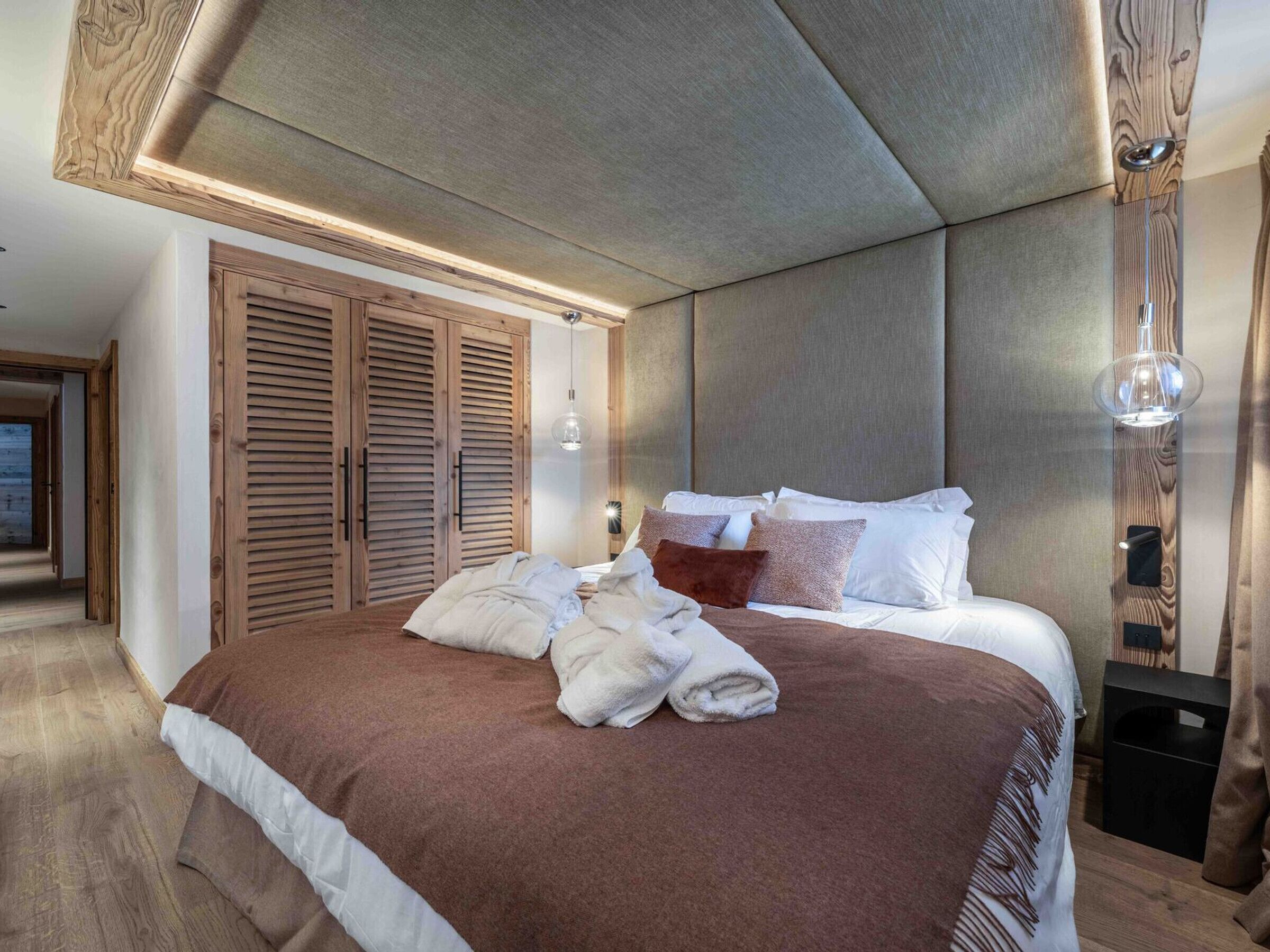 A bedroom with a large bed, wooden wardrobe, and a modern ceiling design.