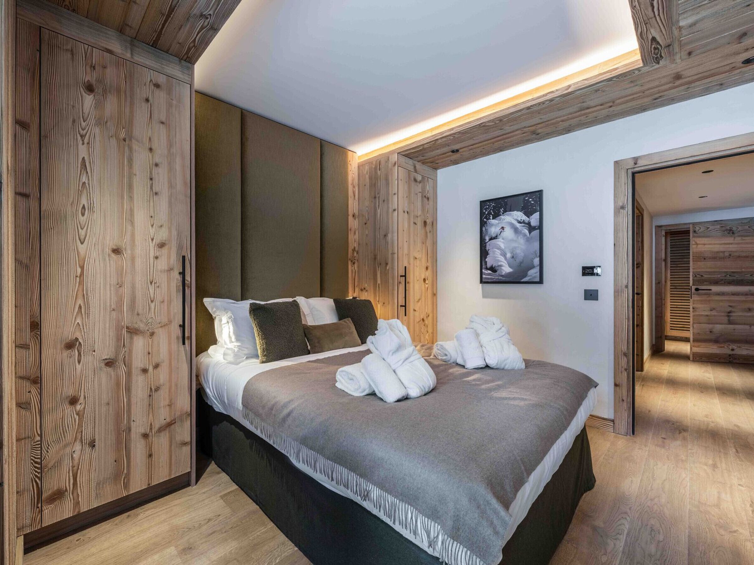 A modern bedroom with a wooden headboard, a bed with white linens, a gray throw blanket, and a framed picture on the wall.