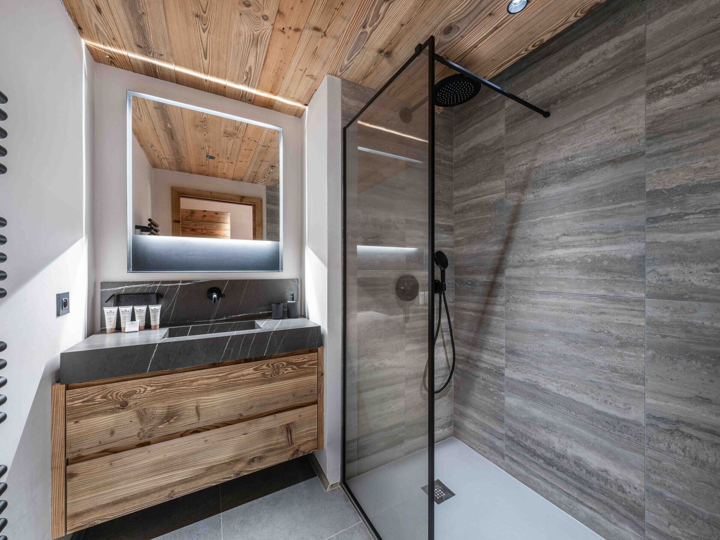 Un baño moderno con tocador de madera, cabina de ducha de vidrio y pared con azulejos de mármol.