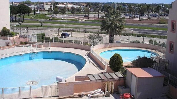 Ein Poolbereich mit zwei Pools, im Hintergrund eine Straße und Gebäude sowie eine baustellenähnliche, abgegrenzte Fläche.