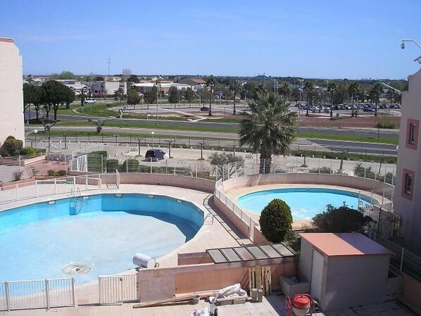 Ein Poolbereich mit zwei Pools, im Hintergrund eine Straße und Gebäude sowie eine baustellenähnliche, abgegrenzte Fläche.