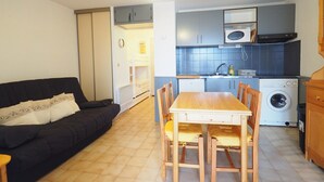 Ein kompakter Wohnraum mit Sofa, Esstisch, Stühlen und einer Küchenzeile inklusive Mikrowelle, Herd und Waschmaschine.