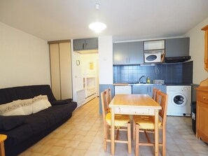 Ein kompakter Wohnraum mit Sofa, Esstisch, Stühlen und einer Küchenzeile inklusive Mikrowelle, Herd und Waschmaschine.