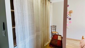 A room with a bed, a chair, a wooden bench, and a curtain.