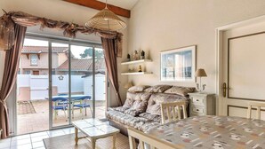 A cozy room with a sofa, a table, and a chair, a sliding glass door leading to an outdoor area with a patio and blue chairs. - Duplex with parking, near beach - 6 guests (Biscarrosse)