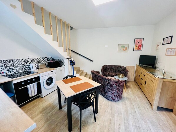 Ett kompakt bostadsutrymme med kök, matplats och en trappa.