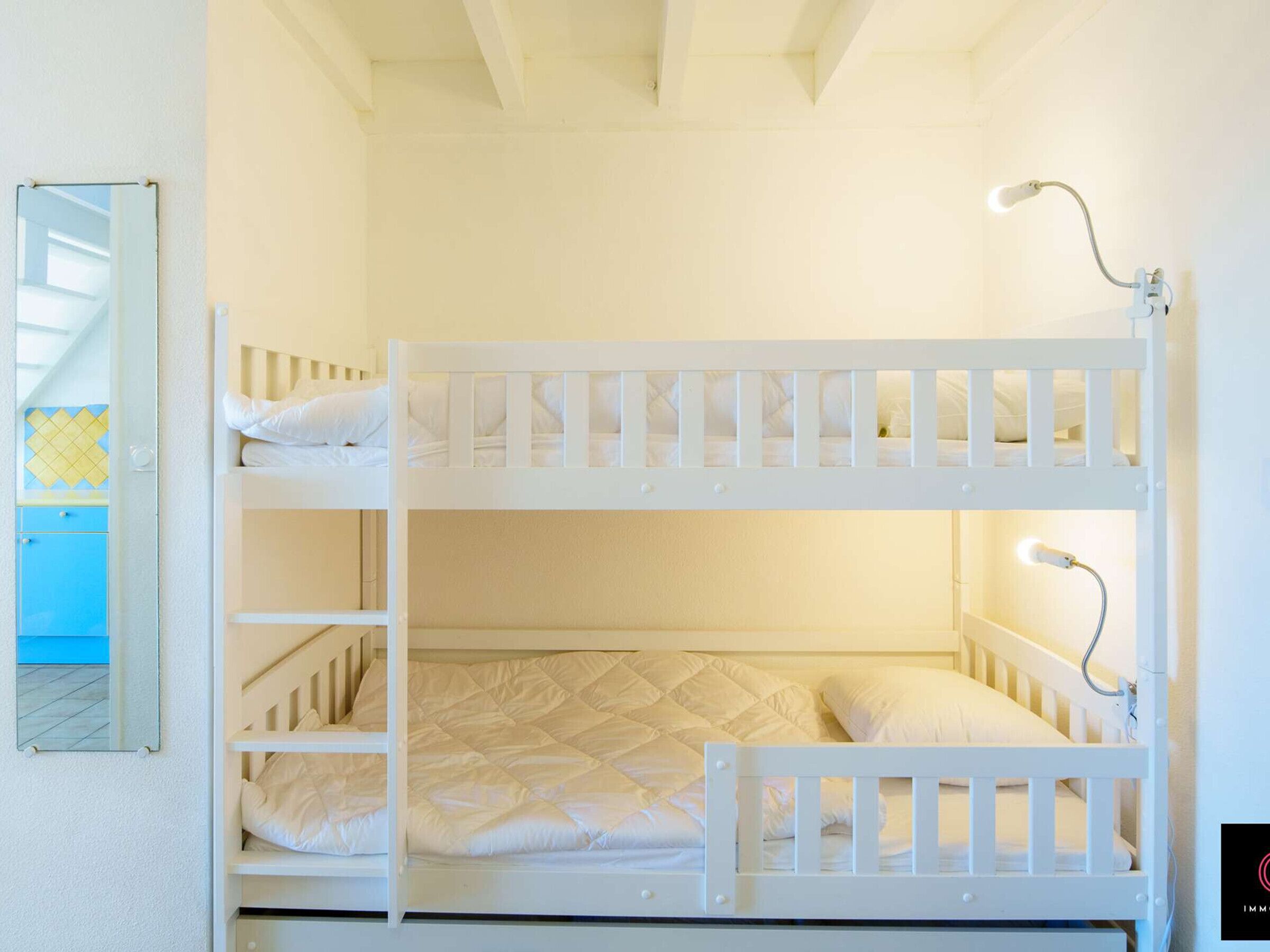 Une chambre avec un lit superposé, un miroir, une lampe de chevet et une armoire bleue.