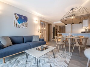 Ein modernes Wohnzimmer mit einer Couch, einem Esstisch mit Stühlen, einer Küchenzeile und einer Deckenleuchte.