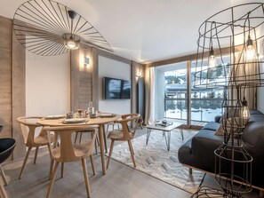 Ein modernes Wohnzimmer mit Essbereich, großen Fenstern mit Schneeausblick und einer außergewöhnlichen Metallleuchte.