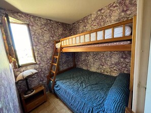 Ein Schlafzimmer mit Etagenbett, Fenster, Nachttisch und Blumenmuster-Tapete.