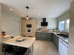 A modern kitchen with built-in appliances, a dining area with chairs, and a window providing natural light. - Villa with pool and pets allowed - 8-10 guests (Vielle-Saint-Girons)