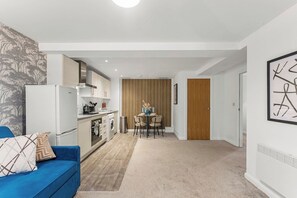 A modern apartment with a kitchenette, a dining area, and a living room with a blue sofa. - Cozy Leeds Hideaway Near the City (Leeds)