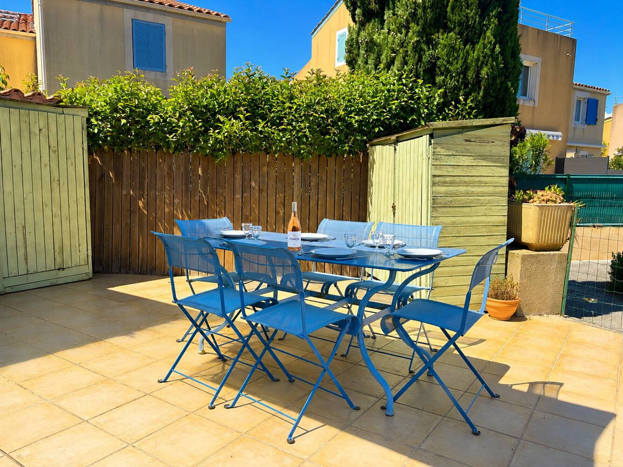 Une terrasse avec une table et des chaises, une clôture en bois et un petit abri de jardin.