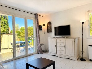 A room with a TV on a cabinet, a table, and a sliding glass door leading to an outdoor area with chairs. - Charming mazet near the beach - 6 guests (La Londe-les-Maures)