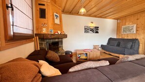 A cozy living room with a fireplace, wooden walls, a sofa, and a couch. - Apartment with panoramic view - 4 guests (Samoëns)
