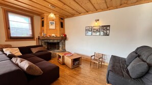A cozy living room with a fireplace, wooden ceiling, and a large window. - Apartment with panoramic view - 4 guests (Samoëns)
