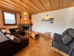 Ein gemütliches Wohnzimmer mit Kamin, Holzbalkendecke und einem großen Fenster.