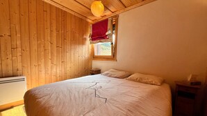 A wooden-paneled room with a bed, a window with a red curtain, and a bedside table. - Apartment with panoramic view - 4 guests (Samoëns)