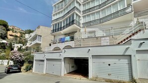 Ein mehrgeschossiges Gebäude mit einer Garage und einer Treppe, die zu den oberen Stockwerken führt. Ein Auto ist geparkt.