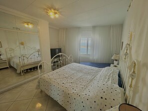 A bedroom with a bed, a television, a window with curtains, and a mirror. - Apartment in Roses with terrace, equipped kitchen and private garage (Roses)