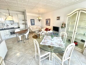 A modern kitchen with white cabinets, a dining area with a glass table, and a living room with a sofa and TV. - Apartment in Roses with terrace, equipped kitchen and private garage (Roses)