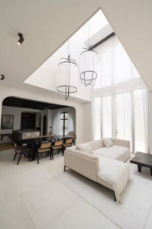 Ein modernes Wohnzimmer mit hohen Decken, einem Essbereich mit einem Marmortisch und einem großen Fenster, das natürliches Licht hereinlässt.