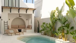 Un área de piscina moderna con una tumbona, un rincón de estar pequeño y diversas plantas.