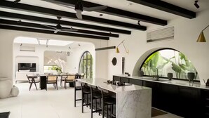 Cocina moderna con una isla de mármol, taburetes negros y un amplio ventanal con vistas a zonas verdes.